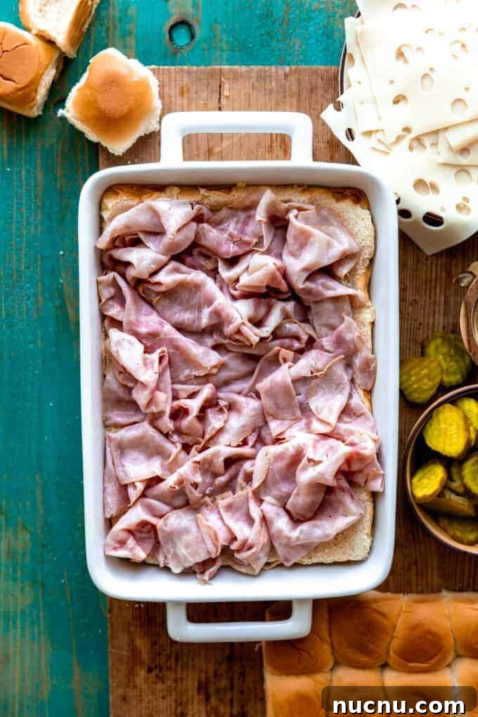 Authentic Cuban Slider Recipe: Mini Cuban Sandwiches to Savor 3 White baking dish filled with a layer of Hawaiian rolls topped with sliced deli ham.