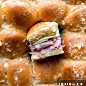 Authentic Cuban Slider Recipe: Mini Cuban Sandwiches to Savor 8 Overhead shot of the tops of sliders with one slider cut out and turned on it's side to show the layers of buns, sliced ham, Swiss cheese and pickles on the inside.