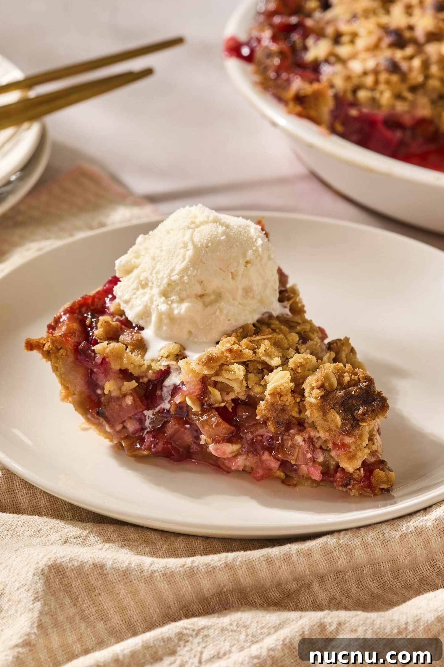 Piece of rhubarb pie on a plate with a scoop of ice cream on top.
