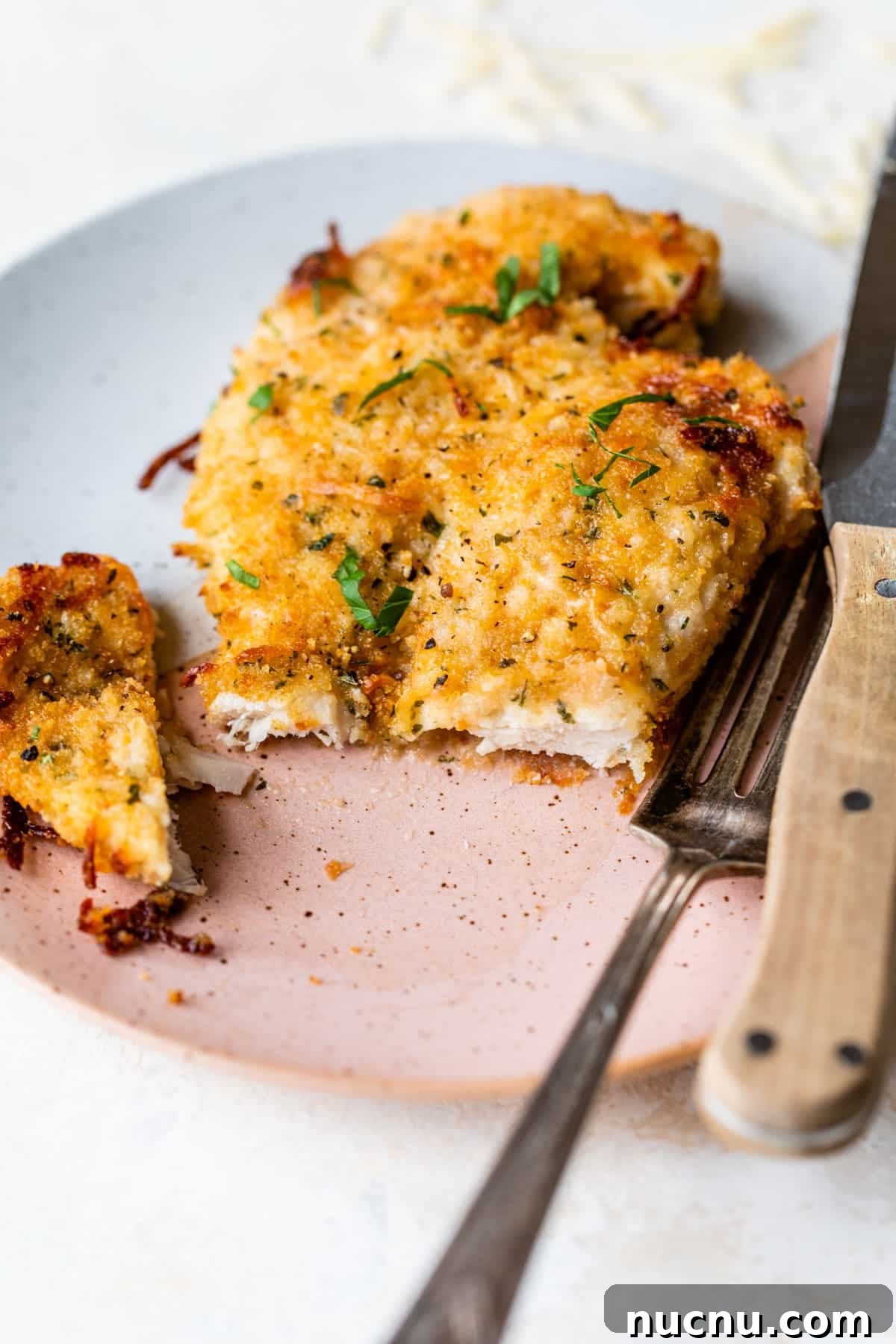 Crispy Baked Parmesan Chicken with Garlic and Herbs 2 baked parmesan chicken with a bite taken out on a plate with a fork