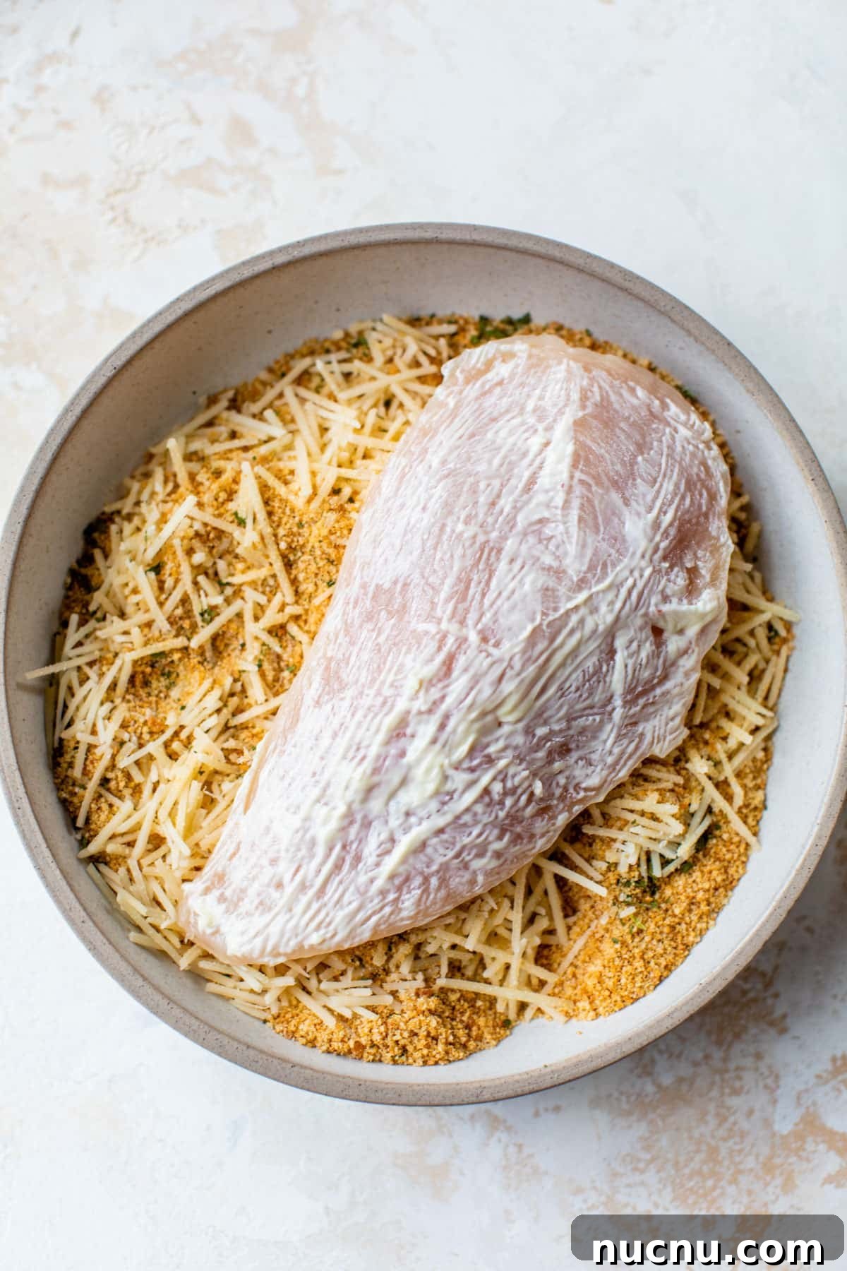 Crispy Baked Parmesan Chicken with Garlic and Herbs 3 raw chicken in a bowl with breadcrumbs and cheese