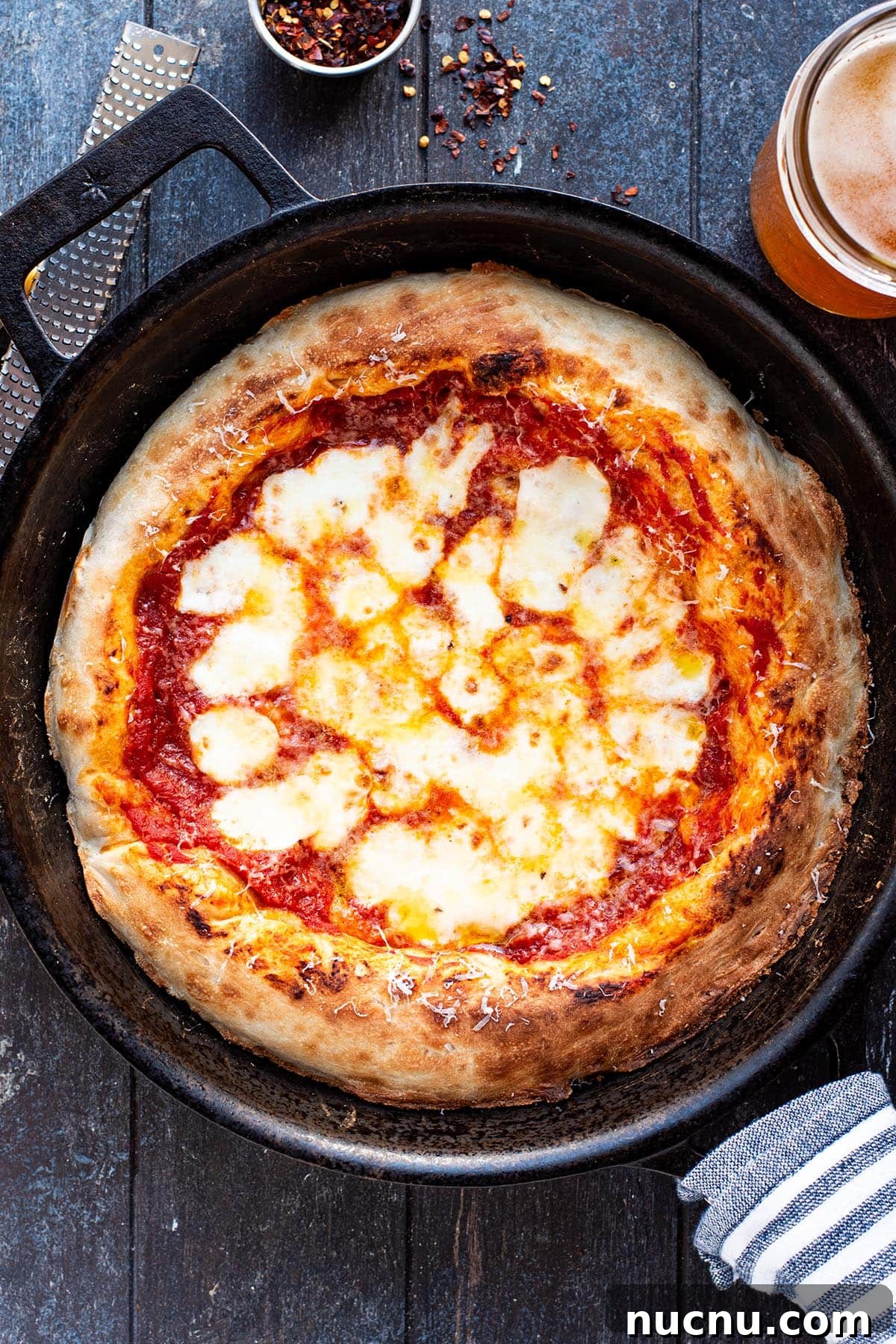 A cheesy golden Margherita pizza in a cast iron skillet on a rustic wooden table.