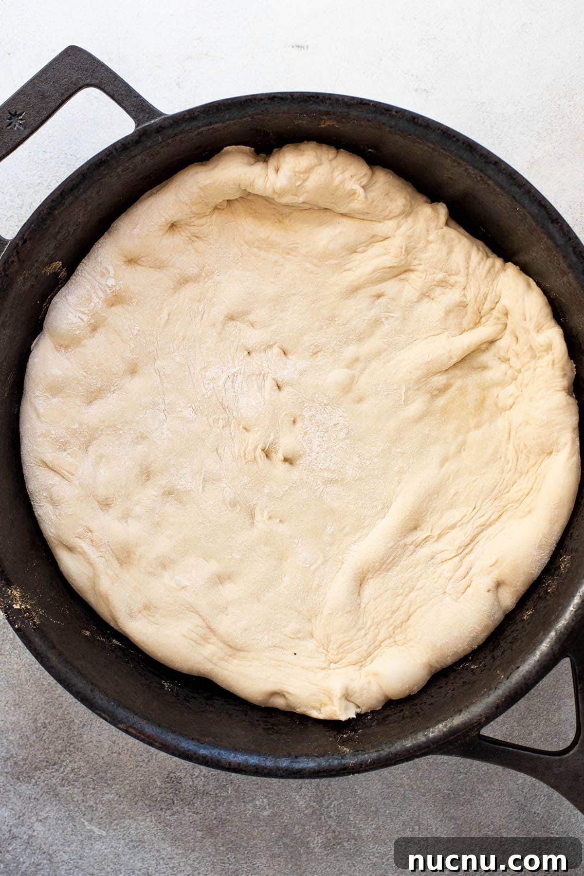An uncooked pizza crust in a cast iron skillet with no toppings.