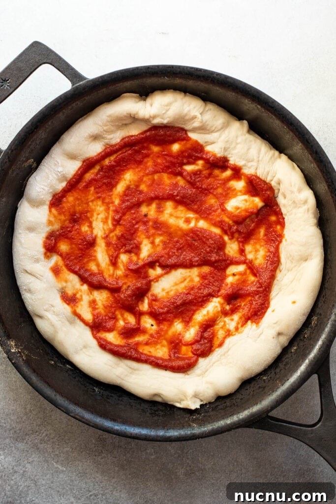 An uncooked skillet pizza topped with fresh tomato sauce.