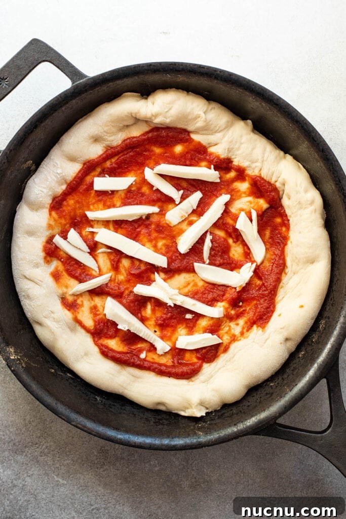 An uncooked skillet pizza topped with fresh tomato sauce and sliced mozzarella cheese.