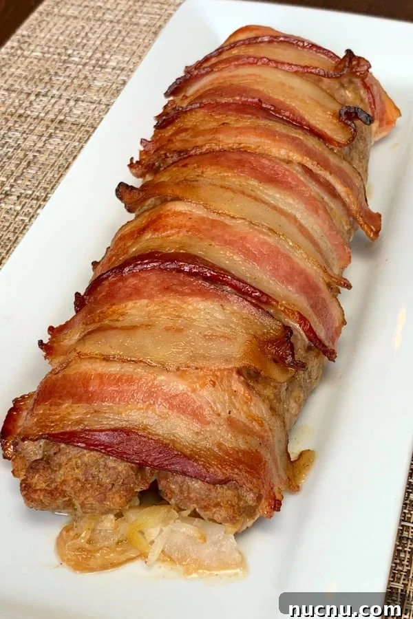 Ground pork roll-up with sauerkraut that's topped with strips of bacon on a white plate and beige placemat
