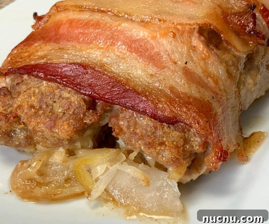 Sauerkraut and onion oozing out of baked ground pork roll-up topped with bacon