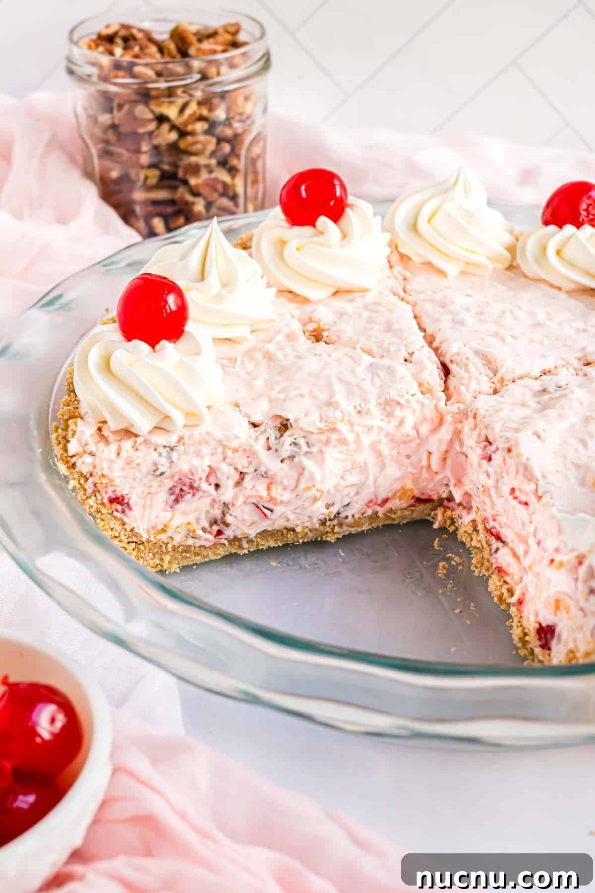 Millionaire pie topped with cherries and whipped cream, one slice removed from pie plate.