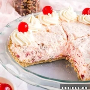 Millionaire pie topped with cherries and whipped cream, one slice removed from pie plate.