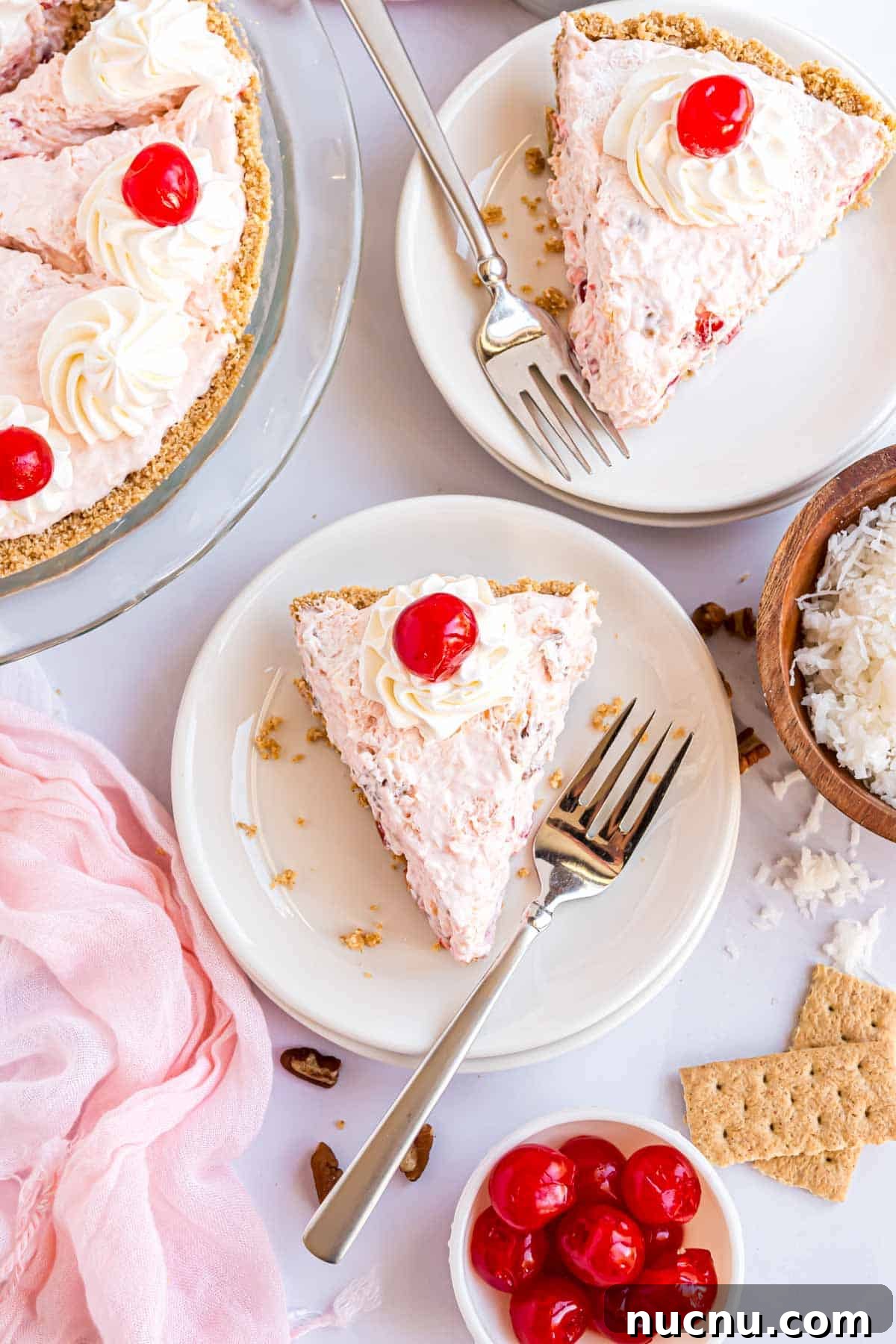 Overhead view of a whipped cream and maraschino cherry topped pie slice on a white plate.