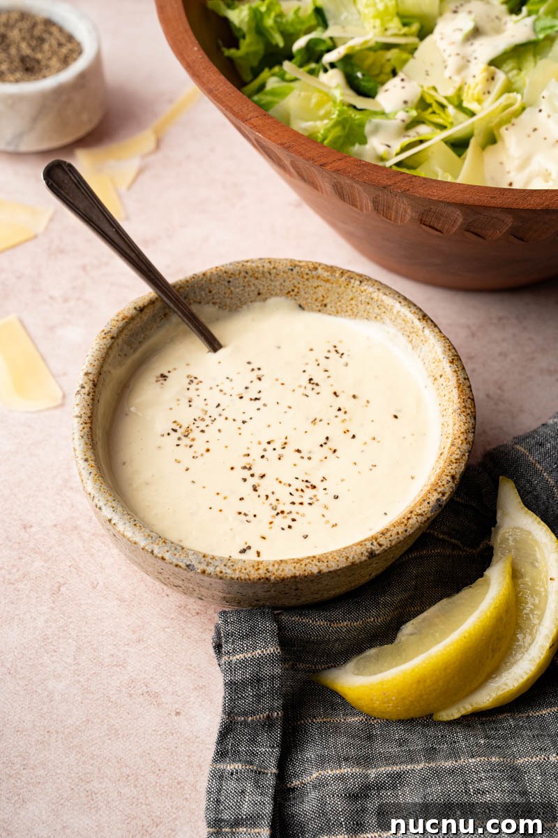Classic Caesar Salad with Creamy Homemade Dressing and Croutons 4 Homemade caesar salad in a small bowl on a countertop next to a bowl of romaine and parmesan cheese.