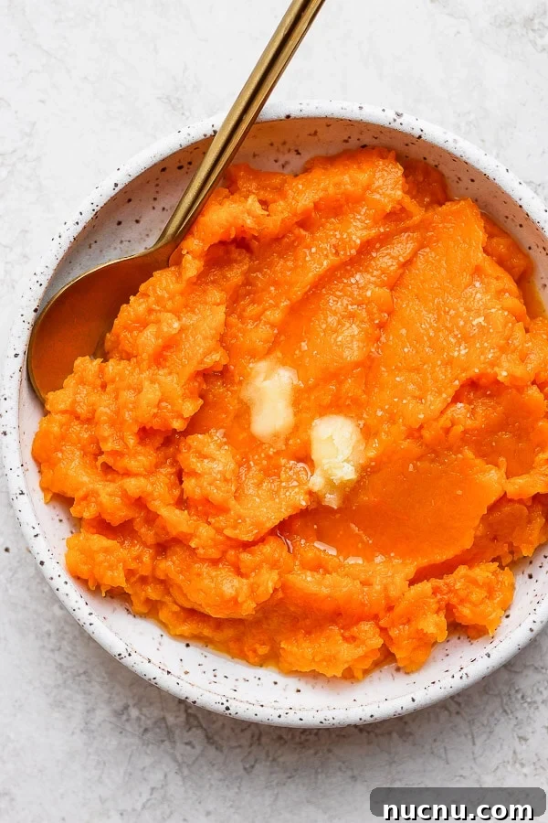 A plate of butternut squash mash with some butter on top and a spoon.