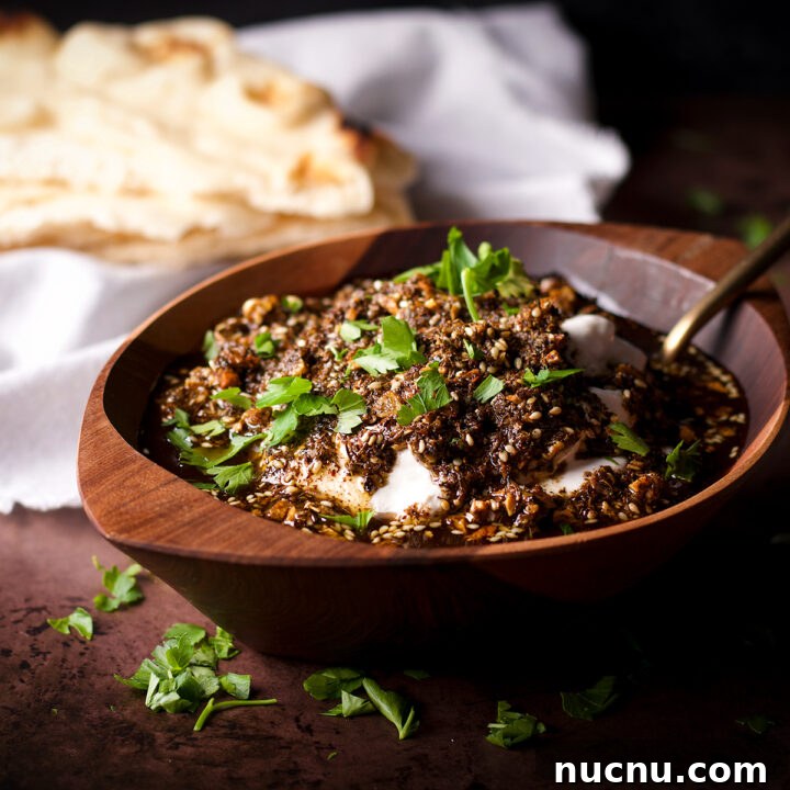 A wood bowl filled with za'atar labneh with crispy garlic sitting next to a stack of buttered naan.