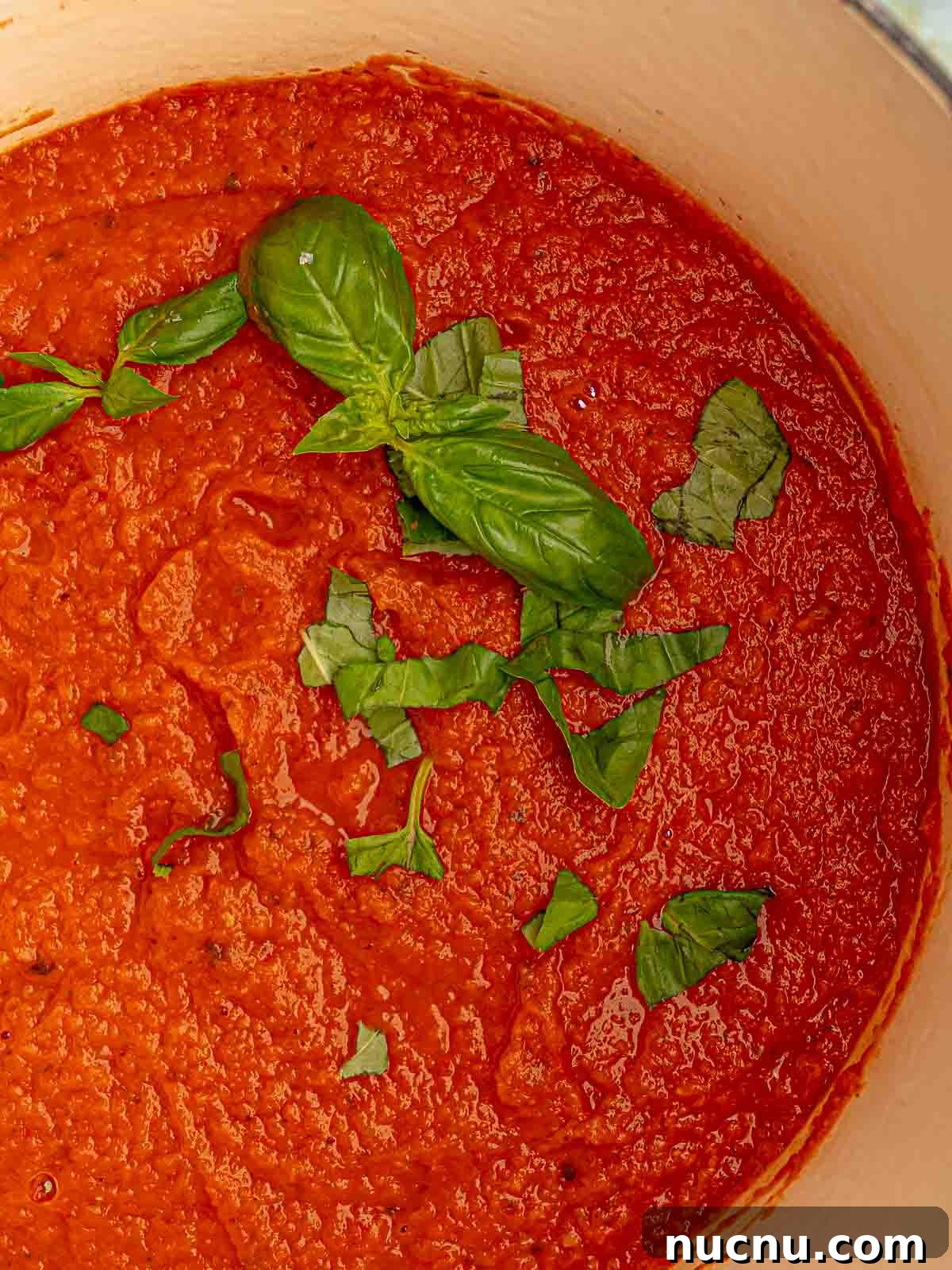 Italian tomato sauce in a pot with basil leaves.