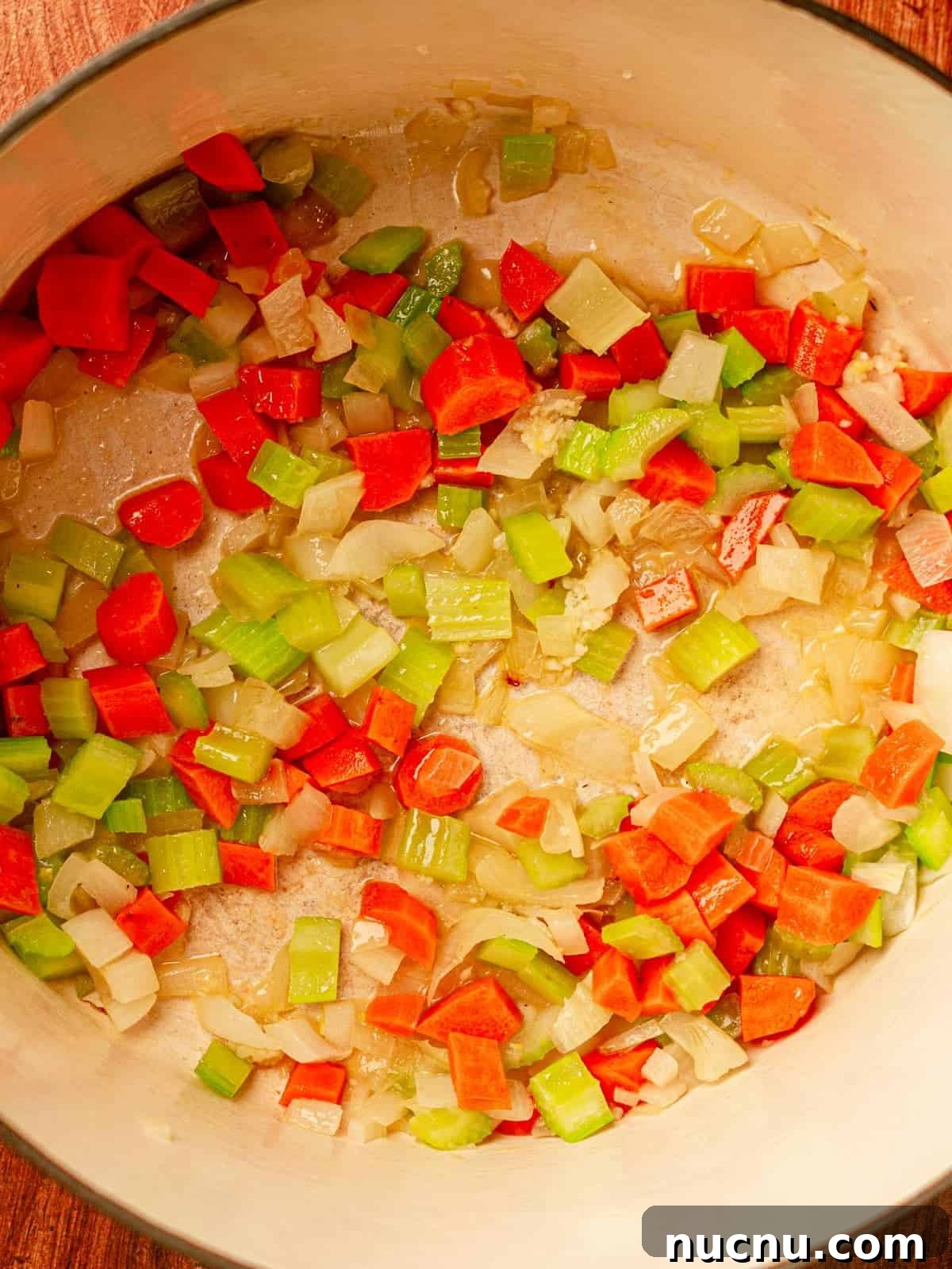 Dutch oven filled with diced and cooked onion, carrots and celery.