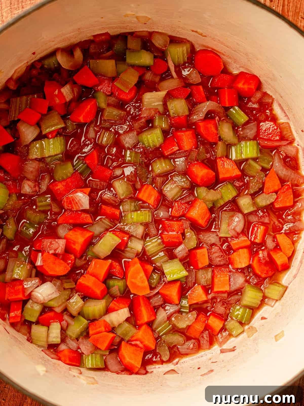 Onions, carrots and celery in a red wine broth in a pot.