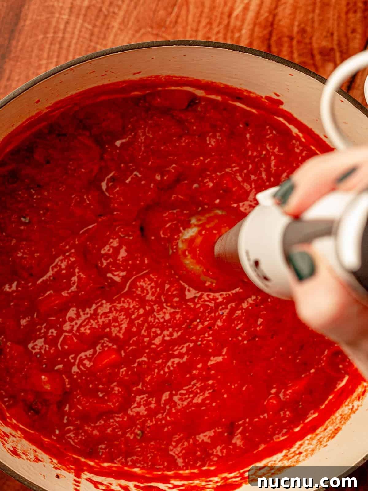 Immersion blender in a pot of tomato sauce.