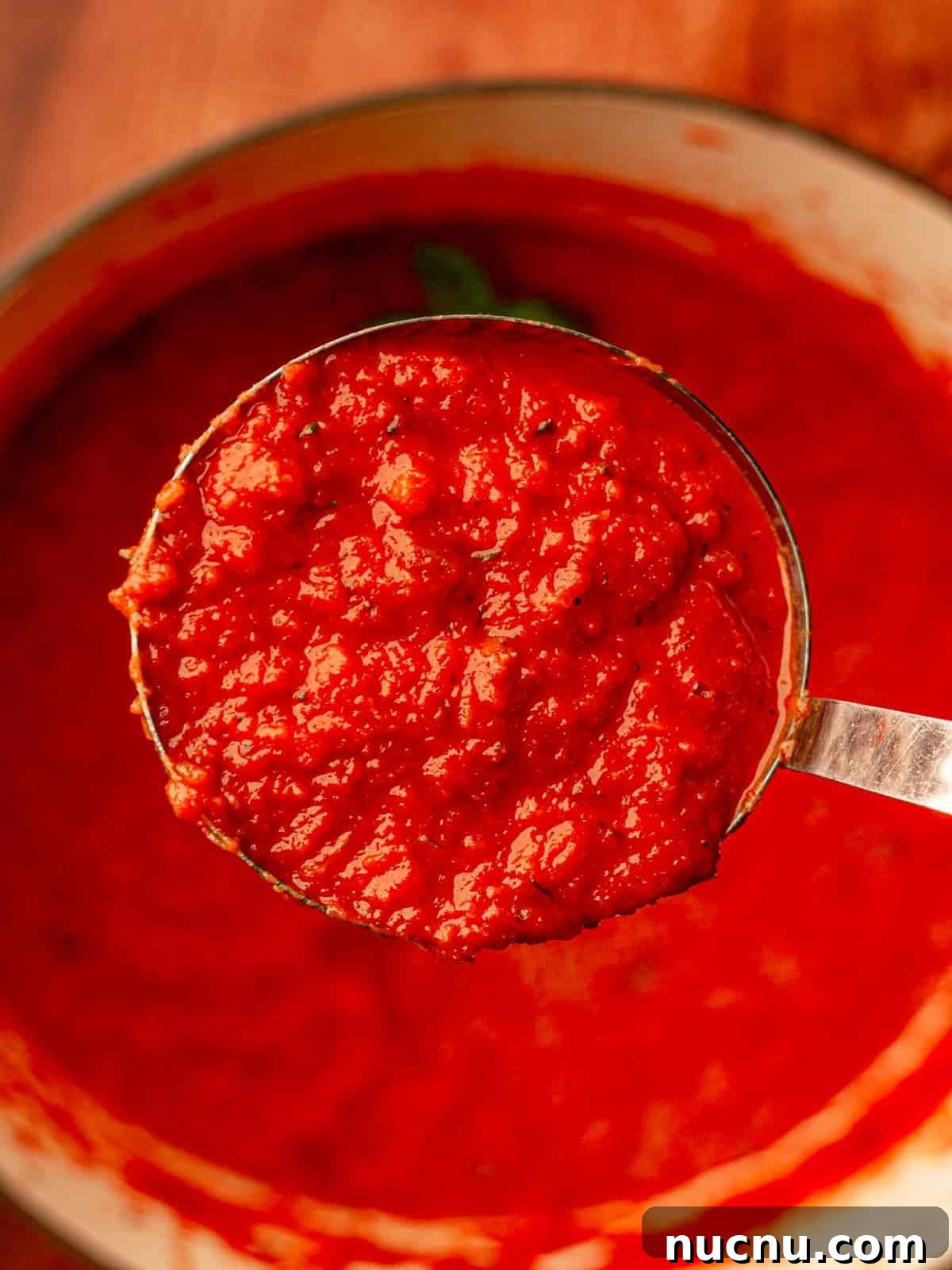 Tomato sauce in a ladle above a pot.