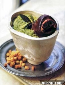 Ham hock and split pea soup in a pottery bowl, garnished with bay leaves, sitting on a plate with a pile of small croutons.