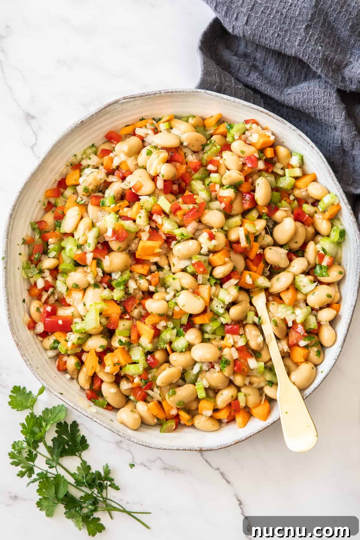 Creamy Butter Bean Salad with Lemon & Herbs — Quick Summer Side 2 Round dish of Butter Bean Salad, with a spoon sitting in it, and a sprig of parsley and grey towel on edge of photo.