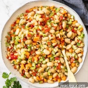 Creamy Butter Bean Salad with Lemon & Herbs — Quick Summer Side 12 Round dish of Butter Bean Salad, with a spoon sitting in it, and a sprig of parsley and grey towel on edge of photo.