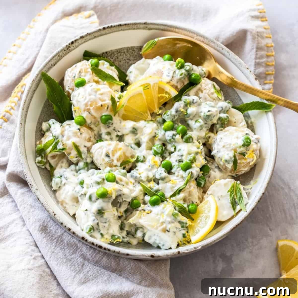 Round bowl of potato salad with a gold spoon in dish, sitting on a cloth.