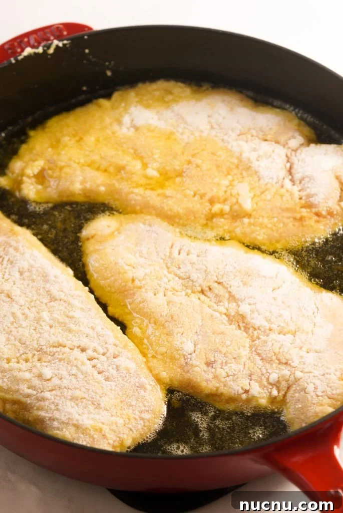 Romano cheese coated chicken breasts pan frying in a large skillet