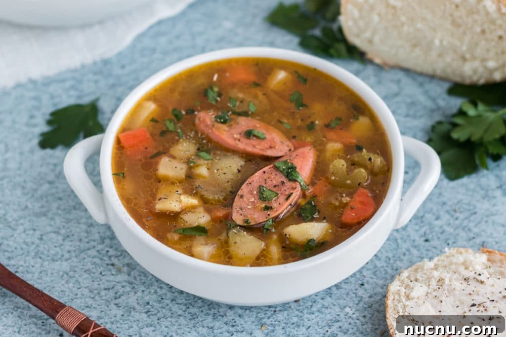 Kartoffelsuppe or German Potato soup in a white bowl with handles on a blue background. The soup has two slices of sausage on top.