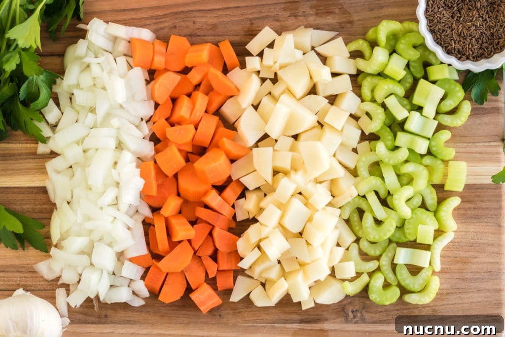Ingredients for Kartoffelsuppe: onions, carrots, potatoes, celery, parsley and caraway seeds on a cutting board.