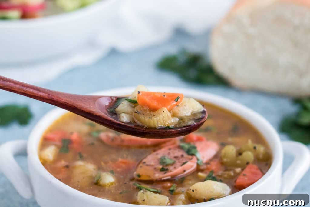 A spoonful of German Potato soup lifted from a white bowl.