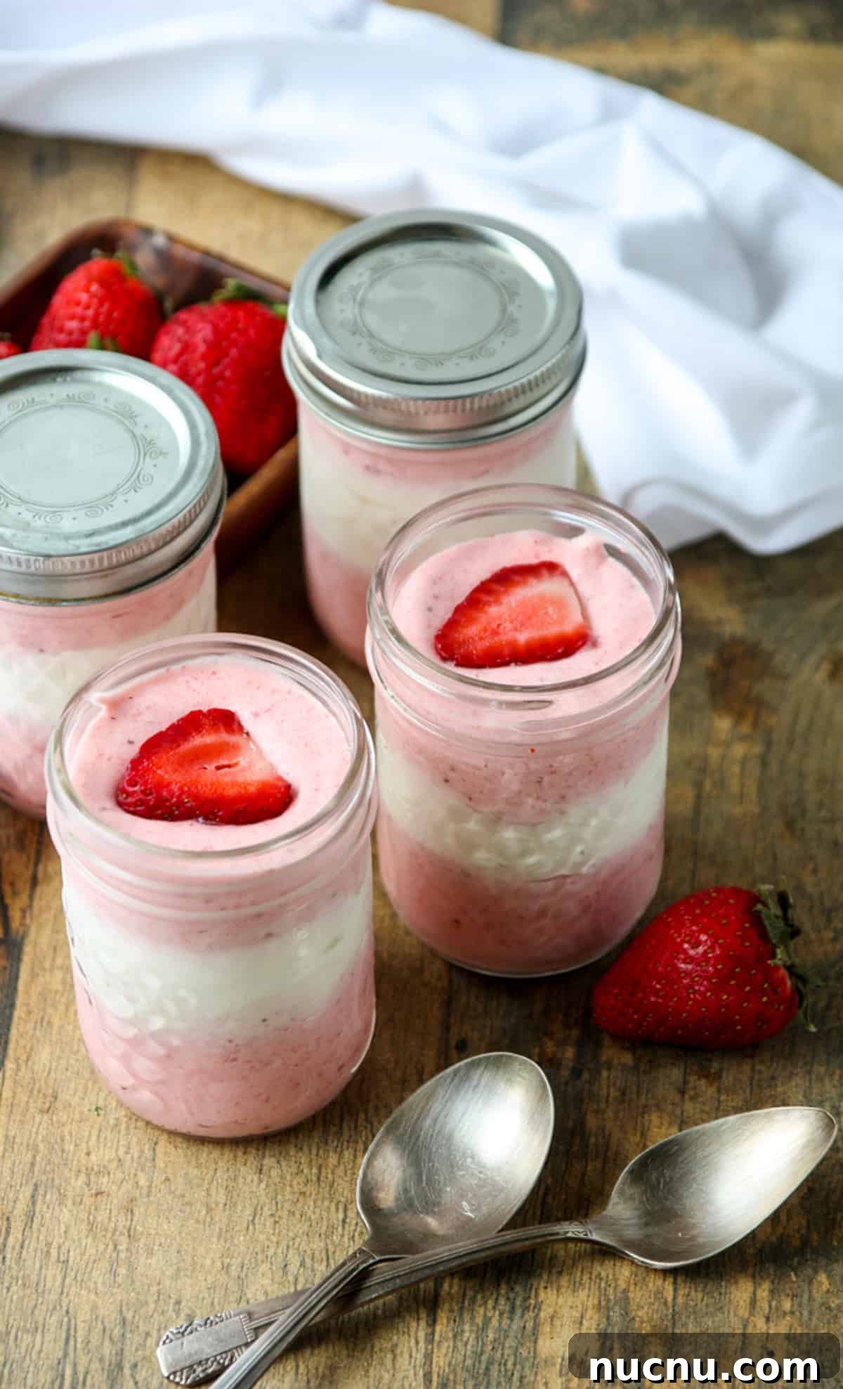 Layered Strawberry Mousse Recipe: Light & Creamy Dessert 4 Four small mason jars filled with the dessert, two with lids, and two silver spoons.