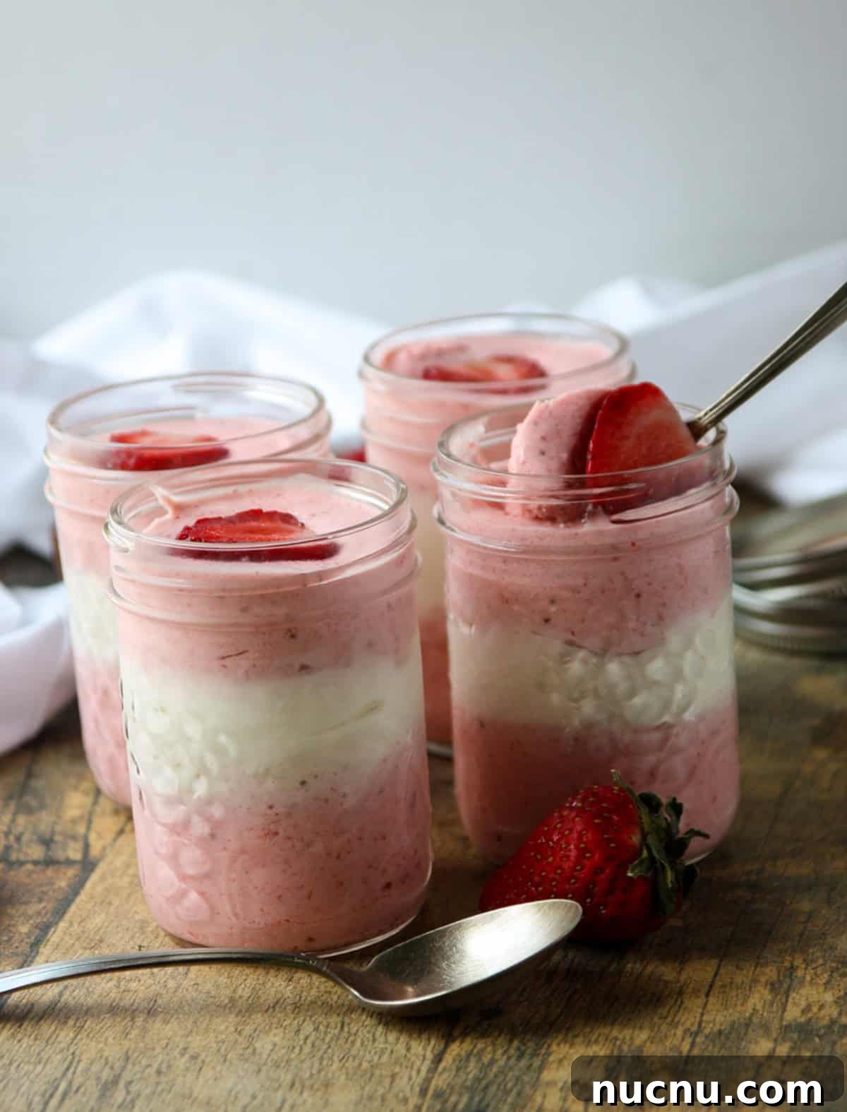 Layered Strawberry Mousse Recipe: Light & Creamy Dessert 5 Four jars of pink and white layered mousse topped with strawberries.