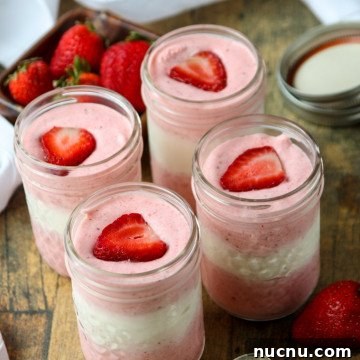 Layered Strawberry Mousse Recipe: Light & Creamy Dessert 7 jars of mousse with pink and white layers topped with fresh strawberry slices in mason jars