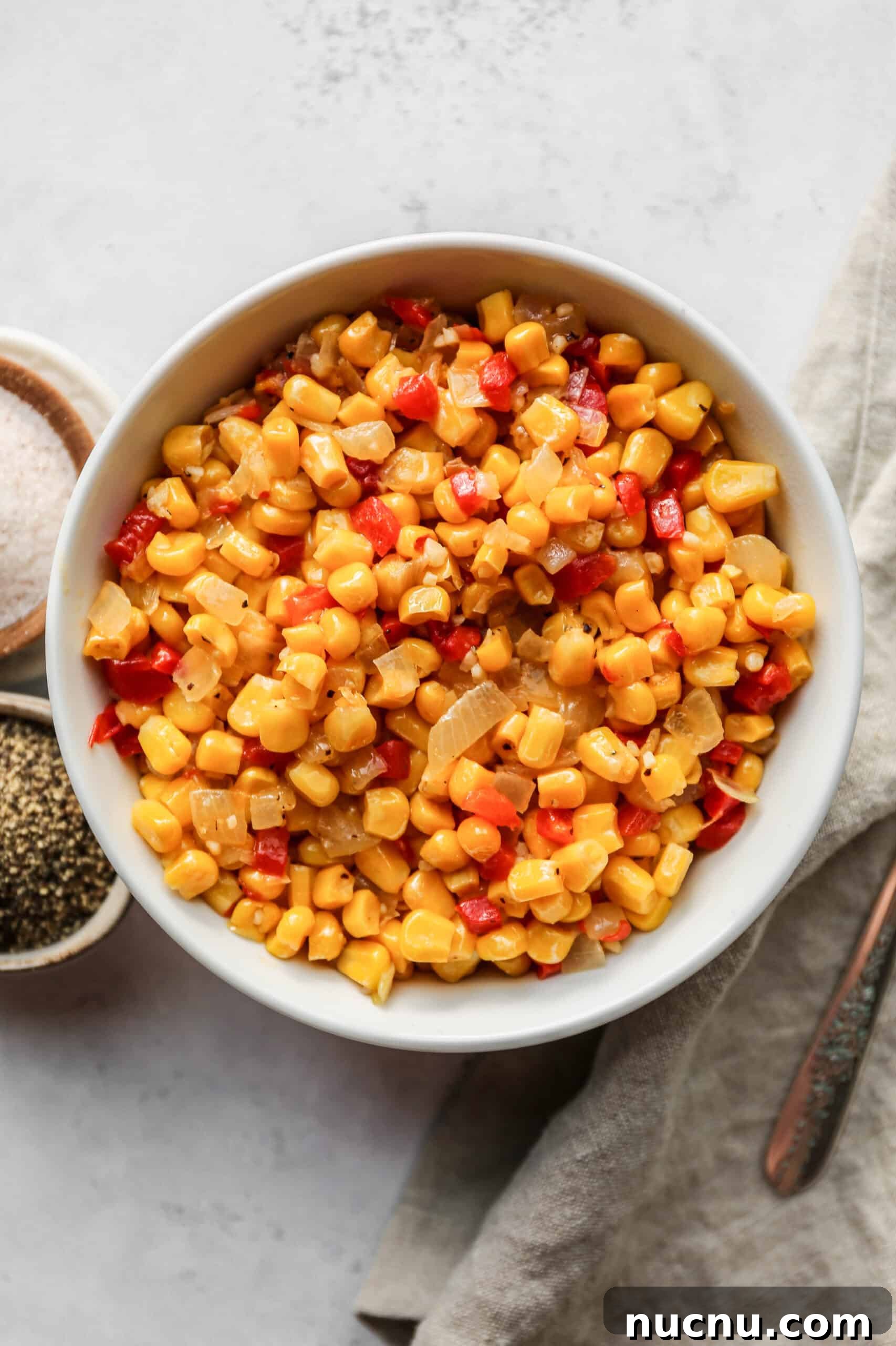 a white bowl of easy fried frozen corn next to small bowls of salt and pepper.