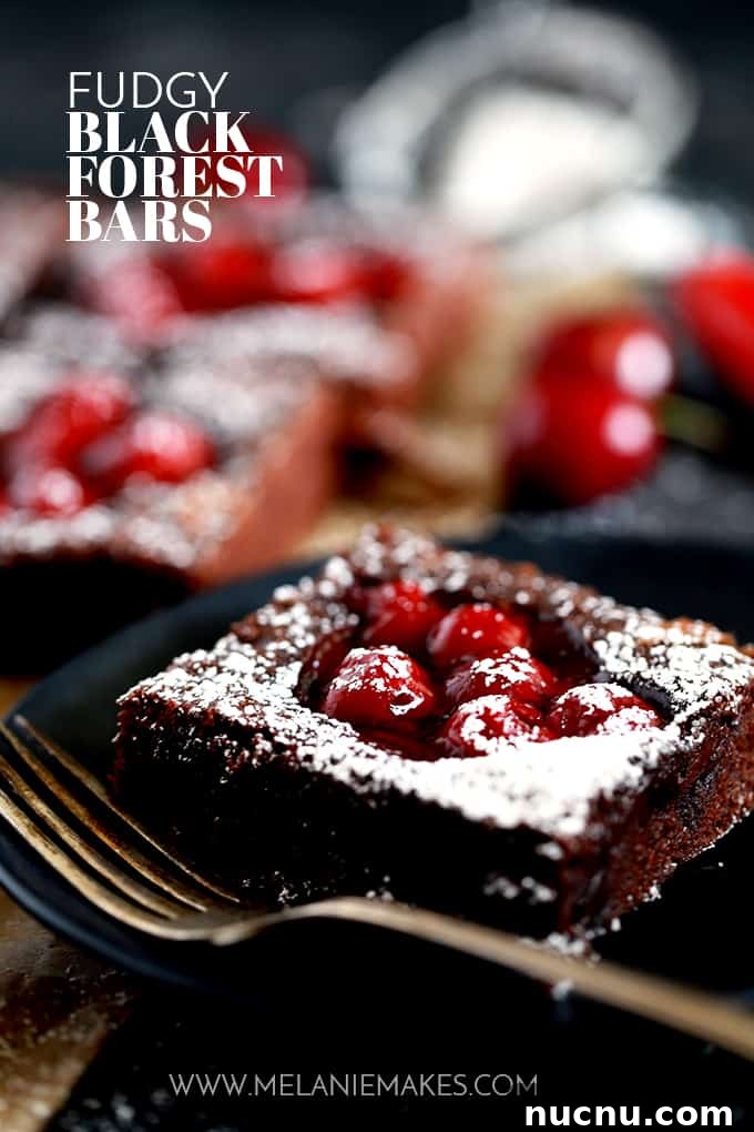 A Fudgy Black Forest Bar sits on a black plate with a fork with additional bars in the background.