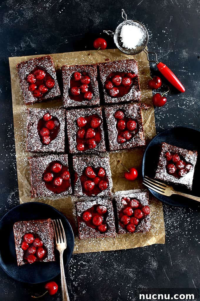 These Fudgy Black Forest Bars definitely have the rich chocolate flavor and moist, dense texture typical of fudge. They’re also the home of puddles of cherry pie filling and studded with dark chocolate chunks before being showered with powdered sugar. The ultimate chocolate and cherry dessert combination. #blackforest #chocolate #cherry #dessertfoodrecipes #desserts Fudgy Black Forest Bars sit on a brown parchment square on a black background. Two bars are on black plates with forks and powdered sugar rests in a sifter.