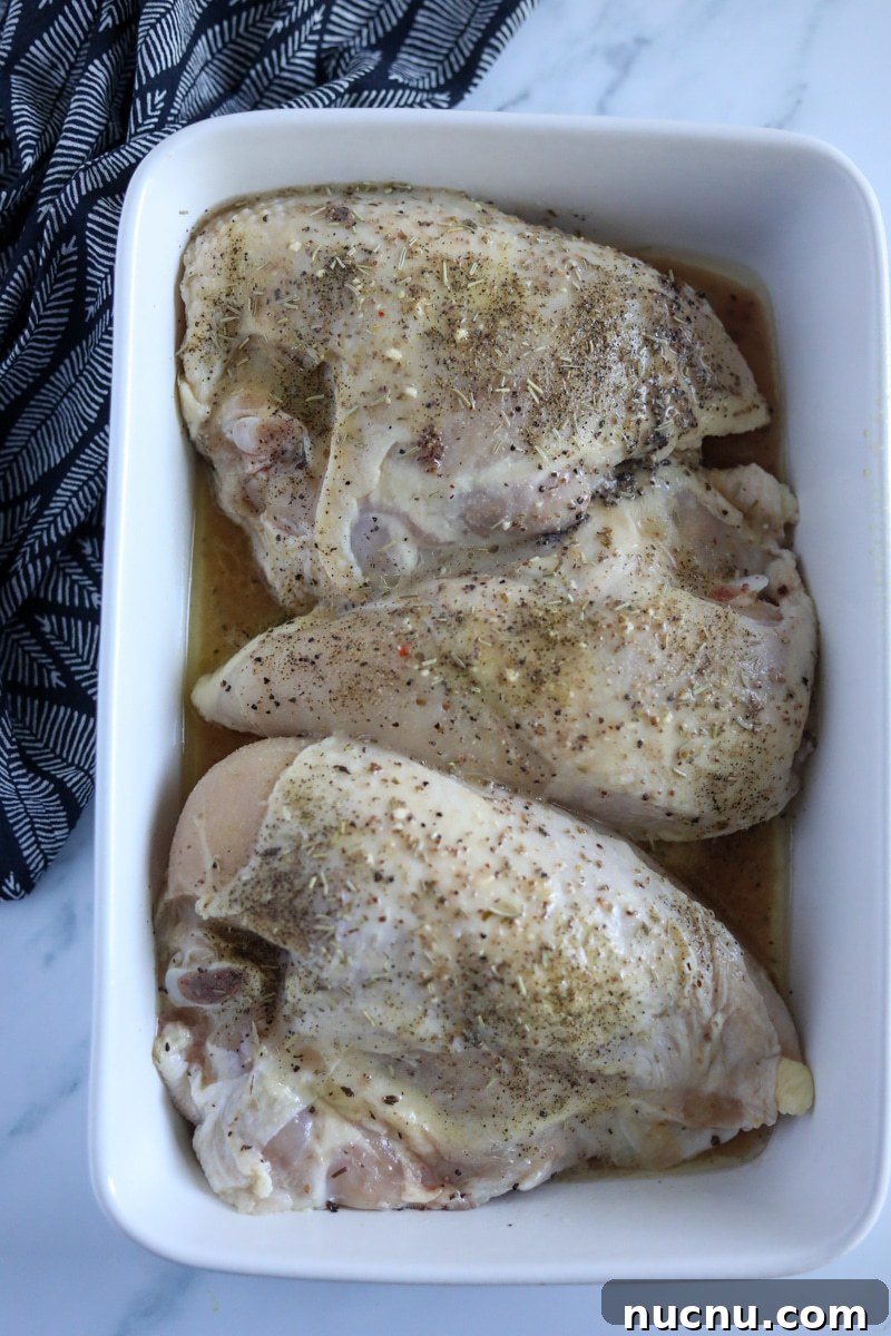 Zesty Italian Chicken and Classic Dressing Recipe 3 raw, seasoned chicken breasts in a glass white dish.