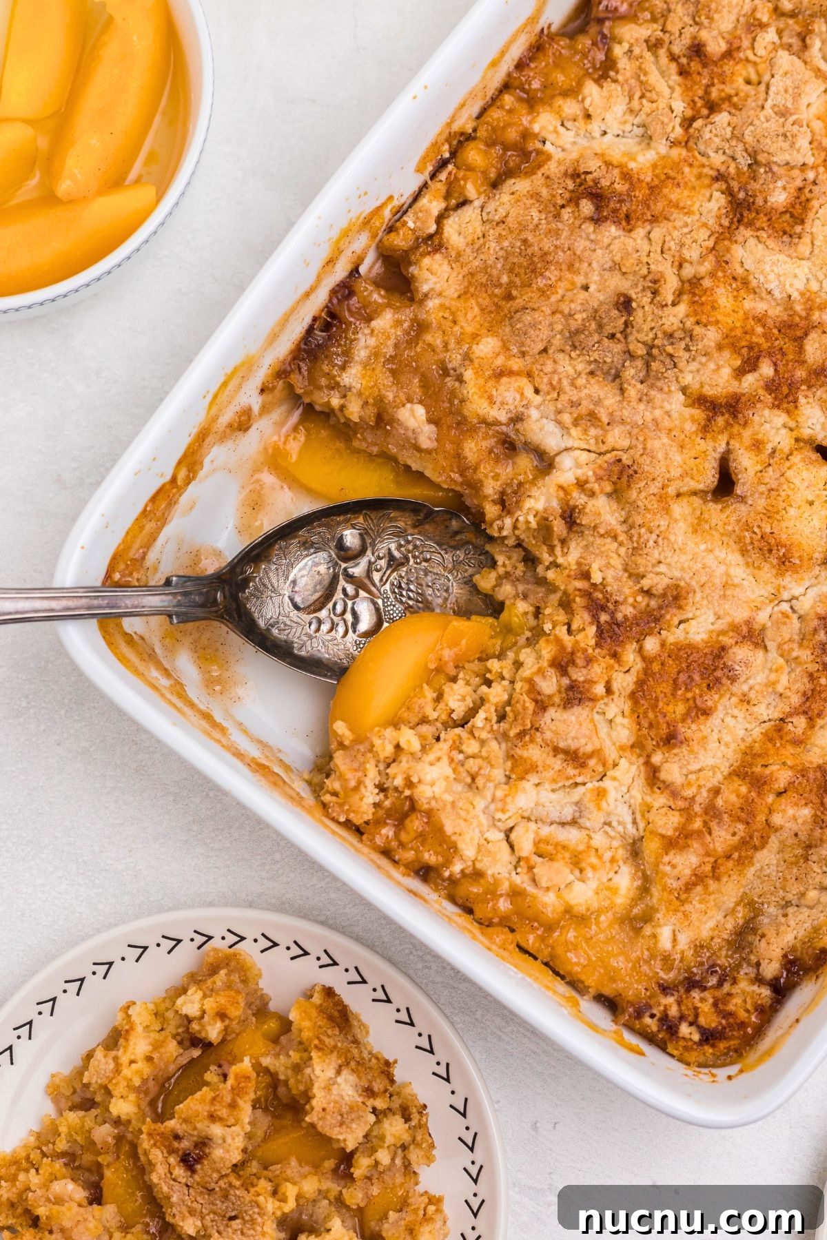 Irresistible Peach Dump Cake Recipe for Quick Summer Desserts 2 Peach dump cake with a slice spooned out onto s small white plate, with the serving spoon in the dish.