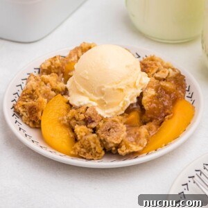 Irresistible Peach Dump Cake Recipe for Quick Summer Desserts 13 Peach cobbler scooped out and served on a small plate, in front of the whole dish, with blue striped straws and cinnamon sticks on the table.