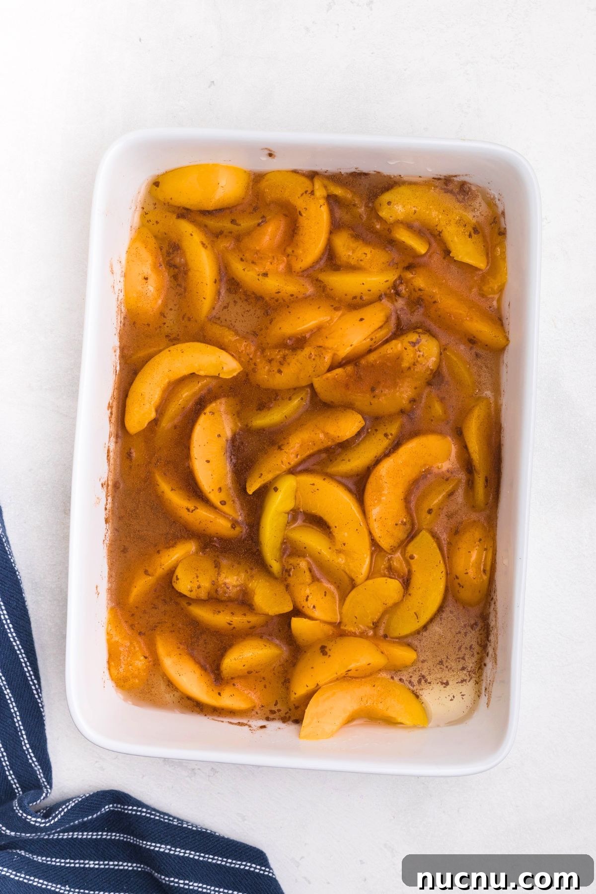 Irresistible Peach Dump Cake Recipe for Quick Summer Desserts 4 White rectangle dish filled with peaches, mixed with cinnamon and vanilla.