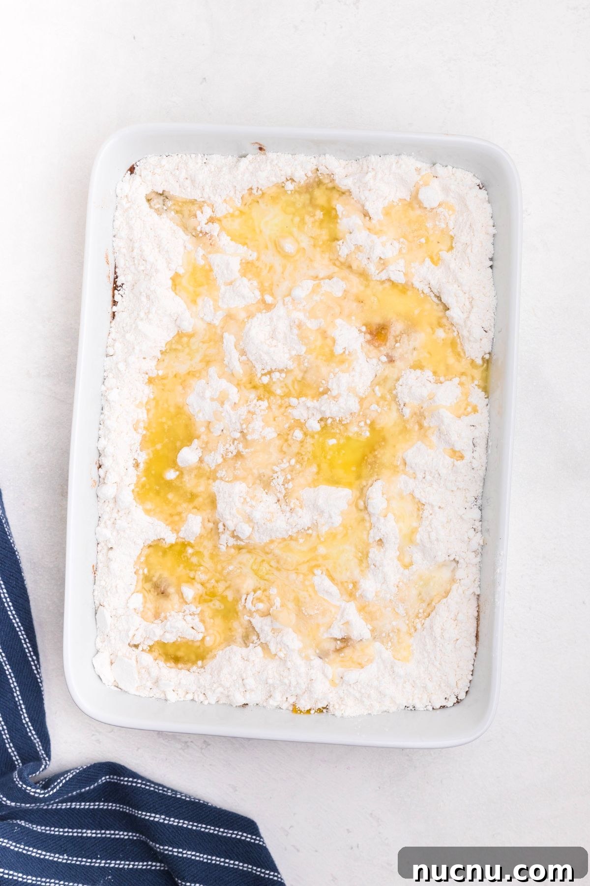 Irresistible Peach Dump Cake Recipe for Quick Summer Desserts 6 Peaches in a white rectangle dish, covered in box cake mix, drizzled with melted butter.