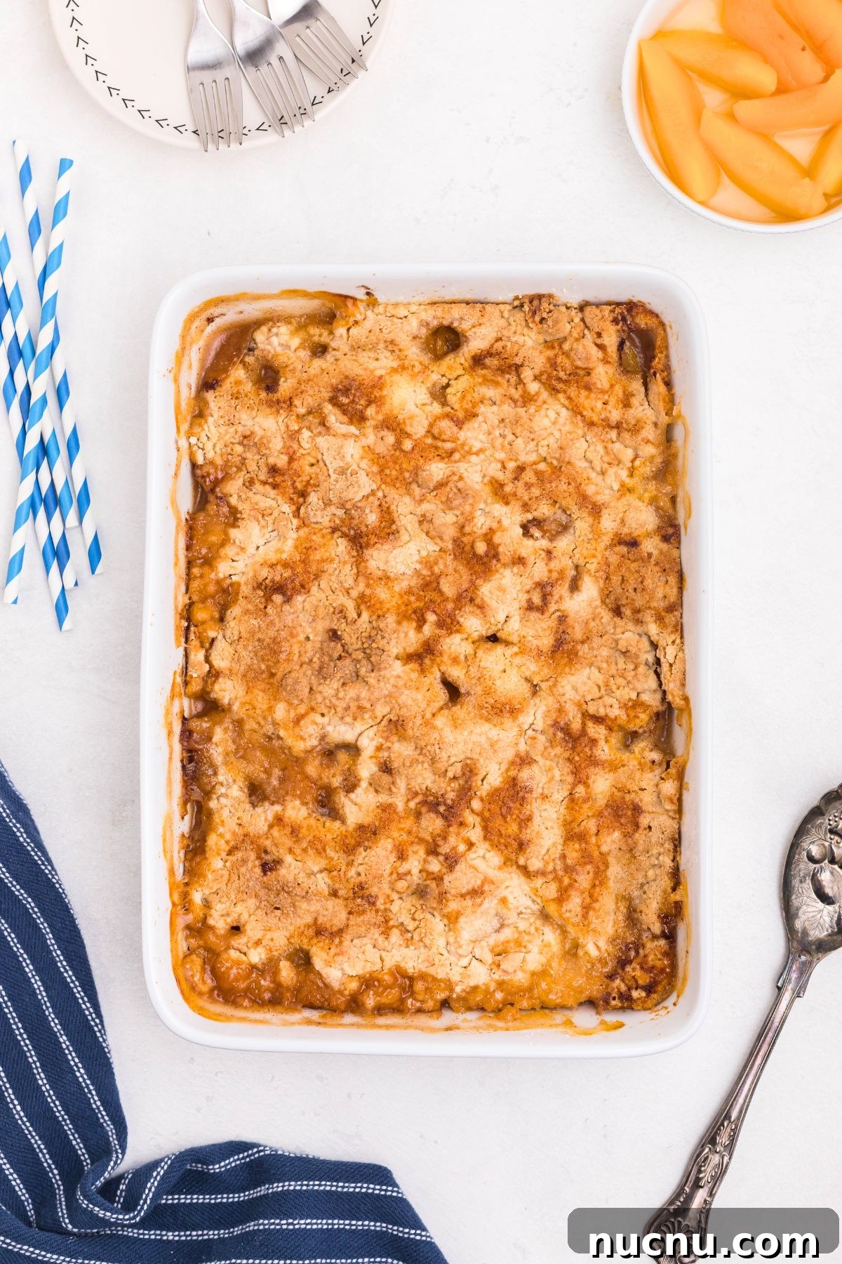 Irresistible Peach Dump Cake Recipe for Quick Summer Desserts 7 Peaches in a white rectangle dish, covered in box cake mix, drizzled with melted butter, then baked until golden brown and bubbly.