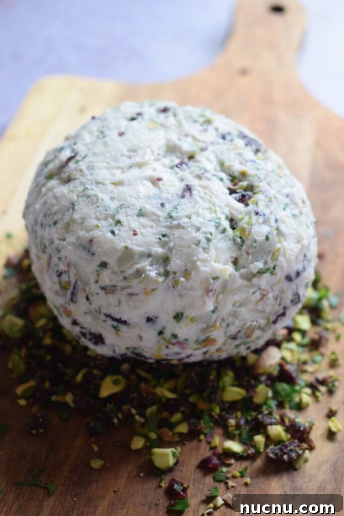 Cranberry Pistachio Goat Cheese Ball Recipe for Parties 13 Cheese ball on a wooden board with nuts and cranberries.