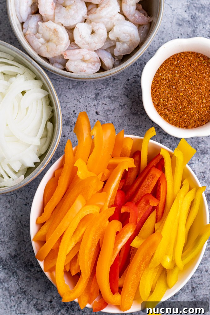 ingredients in separate bowls: bell peppers cut into strips, onion cut into strips, fajita seasoning, shrimp