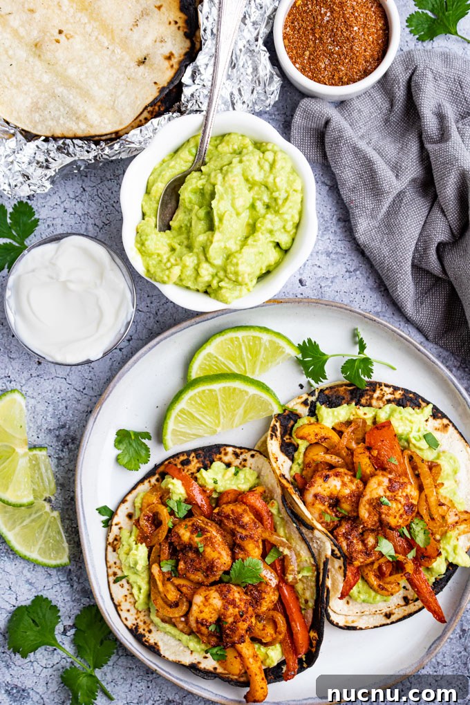 Overhead shot of sheet pan shrimp fajitas. Two shrimp fajitas are made up on a plate with various toppings in bowls.