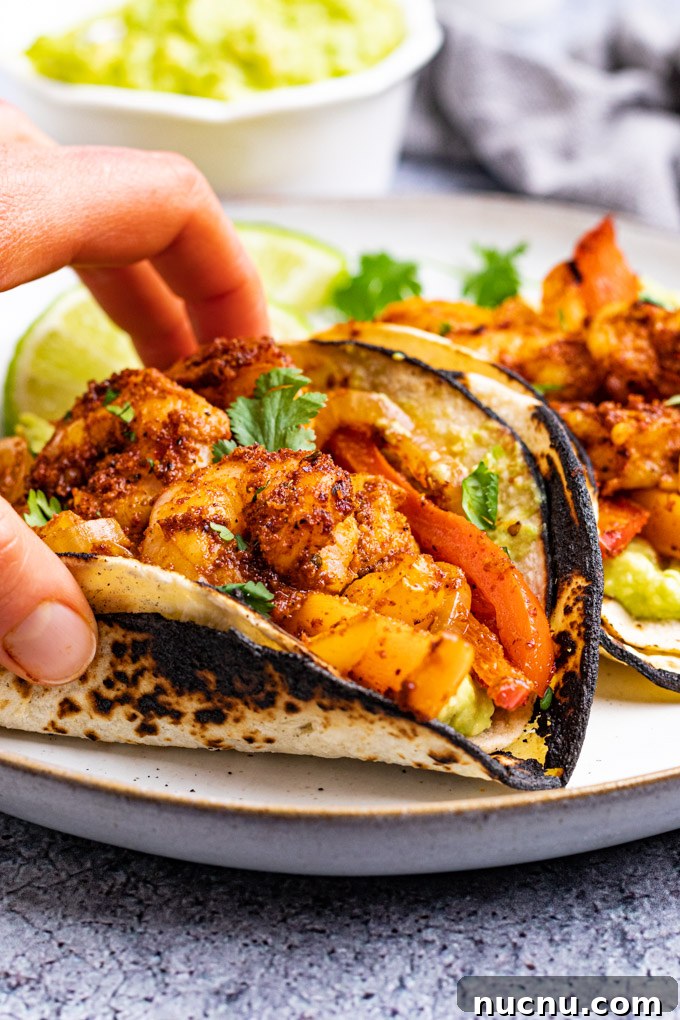 angled shot of sheet pan shrimp fajitas with a hand holding a fajita.