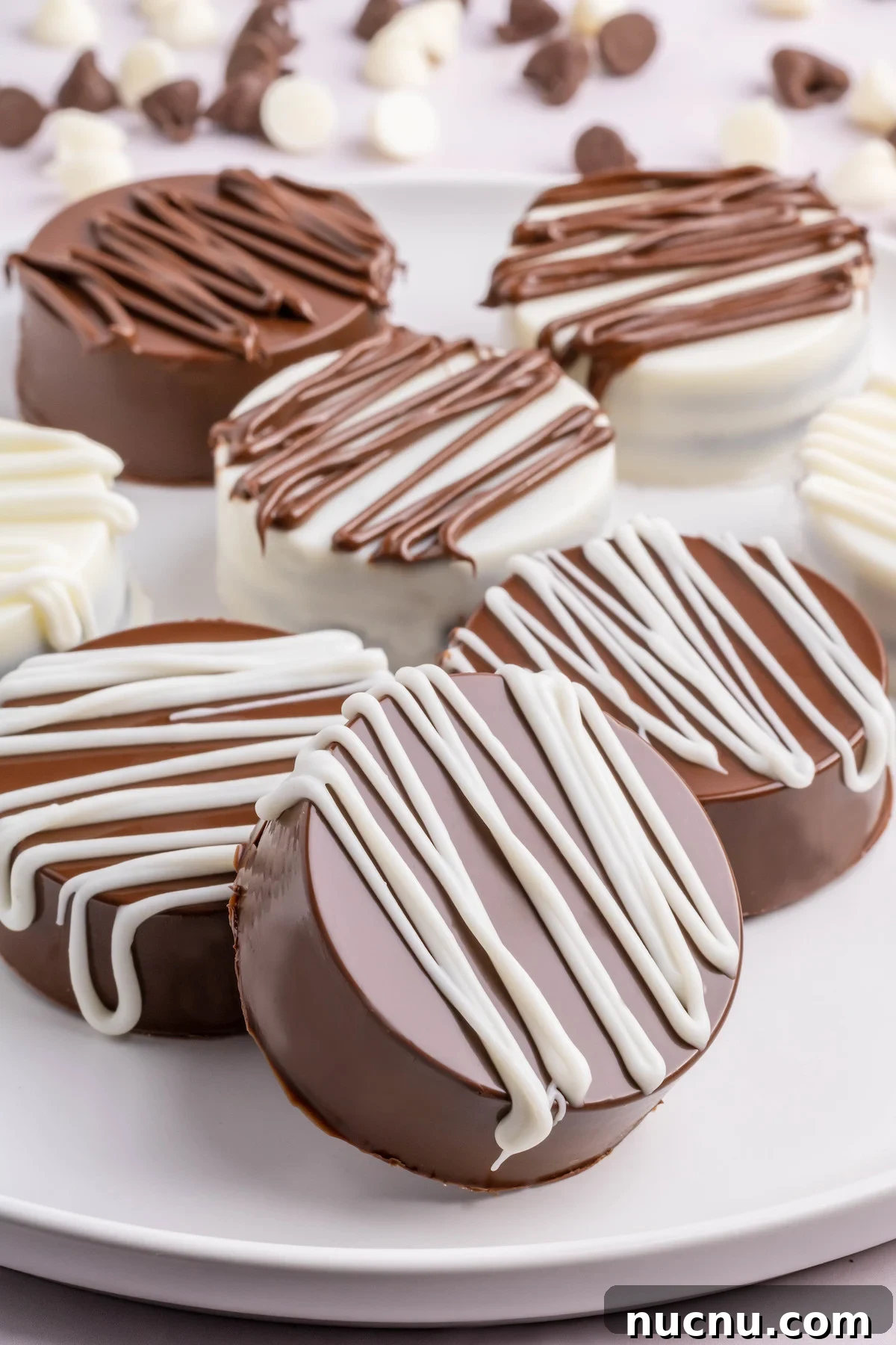 Ultimate Chocolate-Covered Oreos Recipe for Perfect Treats 6 Seven white and milk chocolate covered Oreos on a serving plate. Chocolate chips are out of focus in the background.