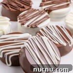 Ultimate Chocolate-Covered Oreos Recipe for Perfect Treats 8 Seven white and milk chocolate covered Oreos on a serving plate. Chocolate chips are out of focus in the background.