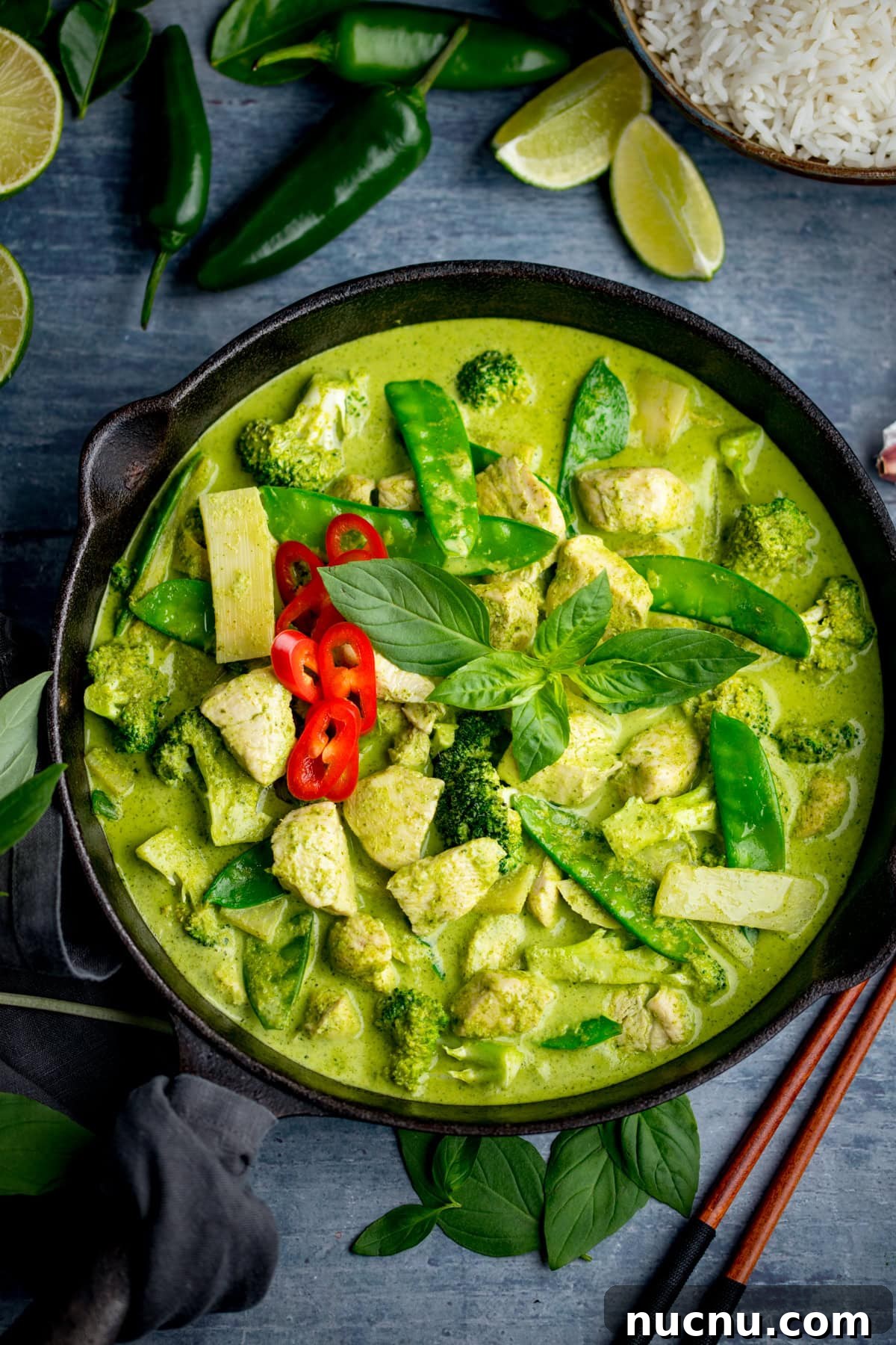 Authentic Thai Green Chicken Curry Recipe (Step-by-Step) 6 A bowl of Thai Green Curry made with authentic Thai green curry paste, featuring chicken, broccoli, bamboo shoots, mangetout, red chilli slices, and fresh basil, served with white rice and lime wedges.