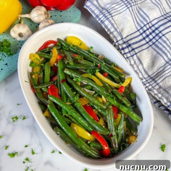 green beans and sweet peppers with bits of garlic on serving plate with parsley garnish
